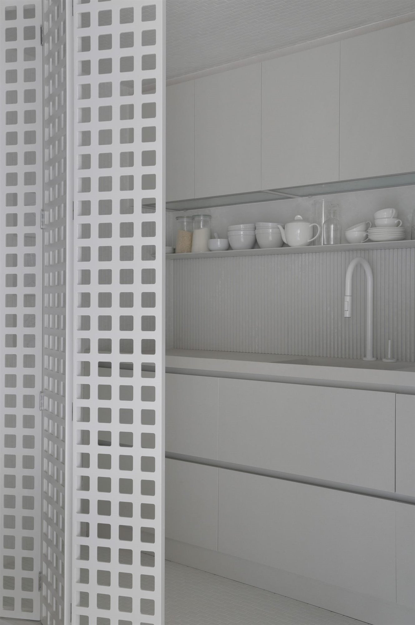 Detalle interior módulo cocina con puerta plegable perforada con motivos cuadrados, encimera, zona de aguas, estantes y amarios