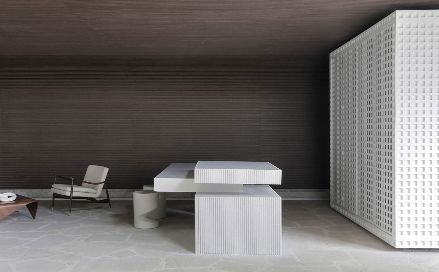 Isla de trabajo con office en cocina, todo en blanco, con mobiliario integrado en estructura independiente y cerrada de acero perforado, butaca en color crema y acabado madera y mesa de centro de madera