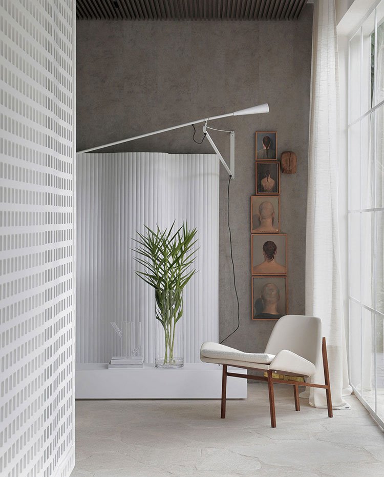 Rincón lectura con butaca en blanco y madera, aplique de pared en blanco a juego con biombo y mueble bajo, revestimiento de hormigón y piedra